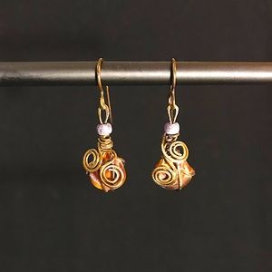 Hand hammered metal wrapped around a dark bead with a small purple bead atop.